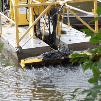 We use a hydraulic dredge to remove the sediment from the pond.  The operator lowers the boom to the desired depth. A cutting bar or water jet mixes the sediment with water allowing it to be pumped.